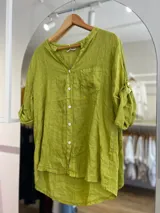 Camisa verde de lino con cuello mao, abotonada al frente y mangas 3/4 con trabillas. Tiene un bolsillo de parche en el pecho y el ruedo es más largo en la espalda.