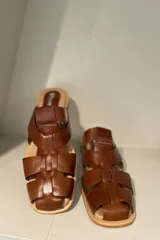 Zueco marrón de cuero vacuno con diseño de tiras entrecruzadas y suela plana.