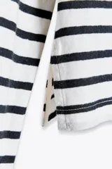 Camiseta de manga larga a rayas horizontales blancas y negras, con cuello redondo y bajo con aberturas laterales.