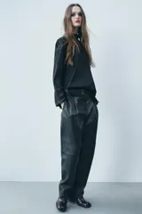 Pantalón de cuero negro de tiro medio, con pinzas delanteras, bolsillos laterales ocultos y corte holgado.