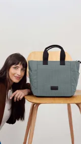 Cartera gris con diseño capitoneado, doble asa corta negra y correa larga ajustable. Tiene bolsillos laterales y un bolsillo frontal espacioso.
