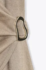 Vestido midi color beige, de corte recto, con escote en pico cruzado, sin mangas y detalle de hebilla metálica en la cintura.