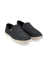 Mocasín de cuero color marrón con cordones decorativos y suela blanca.