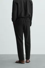 Pantalón negro de corte regular fit, con bolsillos laterales y bolsillos traseros de vivo. Presenta un bajo con vuelta y cierre frontal con cremallera y botón.