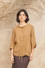 Campera color ocre de lino con cuello mao, cierre frontal con botones, mangas 3/4 con puños abotonados, ajuste con cordón en la cintura y bolsillos laterales.