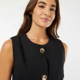 Vestido corto negro sin mangas con botones dorados al frente.