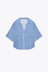 Camisa cropped de viscosa y lino a rayas verticales azules y blancas. Tiene cuello solapa, escote pico, manga corta con vuelta y bolsillos de plastrón.
