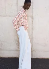 Camisa de manga larga color blanco con estampado abstracto en color ladrillo, cuello camisero y cierre frontal con botones ocultos.