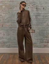 Conjunto deportivo marrón de dos piezas: campera con cremallera, cuello alto, mangas largas con puño y detalles de rayas blancas en mangas y laterales del pantalón. Pantalón recto de cintura alta con cordón ajustable.