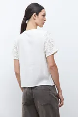 Blusa de manga corta color crudo, con cuello redondo y diseño de encaje bordado floral.