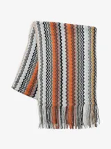 Bufanda rectangular con flecos en los extremos, tejida en punto zigzag multicolor con predominio de tonos naranja, marrón, blanco y negro.