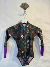 Traje de baño enterizo de lycra con estampado de hojas y flores en tonos verde, marrón y blanco. Tiene mangas largas con puños violetas, cierre frontal con cremallera azul y calce ajustado.