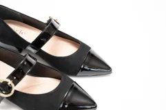 Zapato guillermina de gamuza negra con puntera de charol brillante y tira sobre el empeine con hebilla dorada. Tacón bajo y cuadrado.