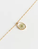 Cadena corta dorada con dije circular transparente que contiene una flor amarilla.