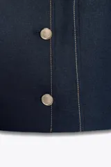 Blazer azul marino de cuello redondo y manga corta, con cierre frontal cruzado con botones dorados y pespuntes decorativos en color crema.