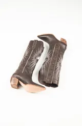 Botas texanas de cuero color marrón con bordados de estrellas y rayos de sol en color blanco. Presentan detalles en rojo en los bordes superiores y un taco de madera. El largo de la caña es de 42cm y la circunferencia de 37cm.