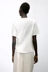 Camiseta blanca de algodón con cuello redondo, manga corta y volantes de gasa en el frente.