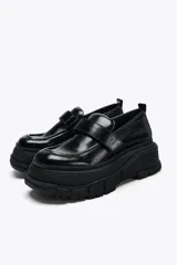 Zapato tipo mocasín negro con plataforma y suela track. Presenta tira ajustable adherente y tirador trasero.