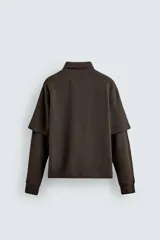 Polo marrón de corte relaxed fit confeccionado en tejido de algodón. Tiene cuello solapa con cierre frontal de botonadura y manga larga con efecto doble manga.