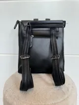 Mochila color marrón de cuero sintético, con asa de mano y correas ajustables. Tiene un bolsillo frontal con cierre a presión y un bolsillo lateral con cierre.
