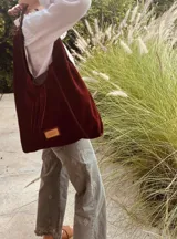 Cartera tipo hobo de gamuza color borgoña con flecos y asa corta de cuero marrón.