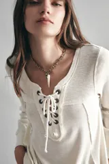 Remera negra de algodón con calce relajado, cuello redondo y mangas largas. Presenta una abertura frontal con arandelas metálicas y cordón.