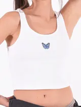 Musculosa corta negra de algodón con breteles anchos y escote cuadrado. Presenta un pequeño bordado de una mariposa azul en el centro del pecho.