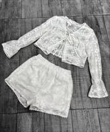 Conjunto blanco de encaje compuesto por un top con mangas acampanadas y cierre frontal con lazos, y un short con cintura elástica.