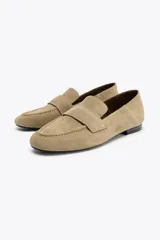 Zapato mocasín color beige de serraje con detalle de tira en la parte delantera y acabado en punta redonda.