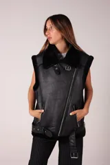 Chaleco negro de eco cuero con cuello y borde de gamulan. Tiene cierre cruzado con cremallera y cinturón con hebilla en la cintura.