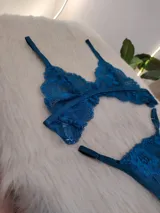 Conjunto de lencería de dos piezas (corpiño y bombacha tipo colaless/tanga) de encaje floral, color verde petróleo/turquesa oscuro. El corpiño es triangular con tirantes ajustables y la bombacha es de corte bajo con bordes festoneados.