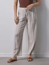 Pantalón de lino a rayas verticales color beige y blanco, con pretina ancha elastizada, lazo de ajuste y bolsillos inclinados.
