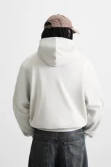 Sudadera con capucha gris confeccionada en tejido de algodón con interior rizo. Tiene manga larga, bolsillo frontal tipo canguro y acabados en rib.