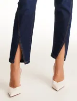 Jean skinny azul oscuro de tiro alto con pierna ajustada, pretina con pasadores, botón y cierre. Cuenta con bolsillos delanteros y traseros, y terminación de ruedo delantero con tajo.