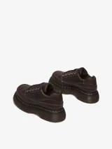 Zapato de cuero marrón con suela gruesa y redondeada, inspirado en modelos de los años 90. Presenta 5 ojales, pespuntes blancos y amarillos, cuello acolchado y cordones tonales.