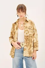 Campera de corte recto confeccionada en gabardina estampada con bordados de hilo. Presenta cuello camisero, cierre frontal con botones, dos bolsillos de parche con solapa en el pecho y lazo ajustable en la cintura con detalle bordado.