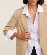 Blazer regular de sastrería color beige, con cuello solapa, sin botón, con bolsillos y detalle de pliegues en las mangas.