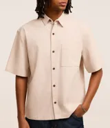 Camisa beige de algodón texturizado, corte boxy, manga corta, cuello inglés y abotonadura frontal.