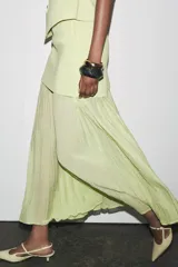 Falda midi color crudo, de tiro alto con cintura elástica y detalle de tejido combinado plisado y semitransparente. Cierre lateral con cremallera oculta en costura.