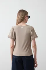 Remera de tejido acanalado color blanco, con cuello redondo y mangas cortas que presentan un detalle de terminación en puntilla en los bordes.