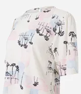 Blusa de viscolino color crudo con estampado de paisaje con palmeras y casas en tonos pastel. Tiene cuello redondo y mangas cortas abullonadas.
