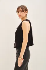 Blusa negra sin mangas, con escote en V profundo y volados en el frente. Tiene lazos en el cuello y gancho invisible para regular el escote.