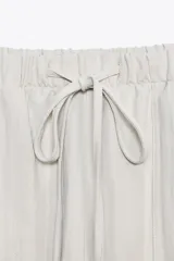 Pantalón jogger color gris claro, de tiro alto con cintura elástica ajustable con cordones, bolsillos delanteros y traseros con solapa, y puños elásticos en el bajo.