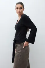 Sweater de tejido de punto negro, con escote en V pronunciado y mangas largas acampanadas. Presenta un lazo ancho anudado a la cintura.