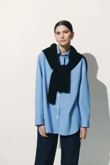 Camisa celeste y blanca a rayas verticales, de corte amplio y mangas largas con puños abotonados. Cuello clásico y cierre frontal con botones.