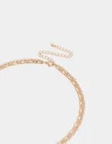 Collar corto multicadena dorada, con una cadena de eslabones y otra de perlas sintéticas con cuentas florales y dije de moño metálico.