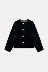 Chaqueta corta de cuello redondo y manga larga en tejido de pelo sintético color negro. Cierre frontal con botones metálicos dorados y bolsillos de plastrón. Colección Zara Woman.