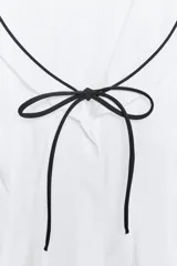Top blanco de popelina con cuello marinero, escote pico, sin mangas y lazo negro en el frente.