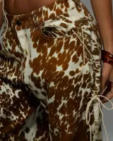 Conjunto de dos piezas (top y pantalón) con estampado que imita piel de vaca en tonos marrón y blanco. El top es tipo corset sin mangas, con cuello alto y lazada frontal ajustable. El pantalón es de tiro alto y corte recto.