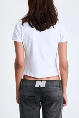 Remera blanca de manga corta con escote redondo y corte cropped. Presenta un estampado frontal de un corazón tridimensional con efecto de rejilla en color rojo y texto cursivo en negro que dice "Too famous for a job".